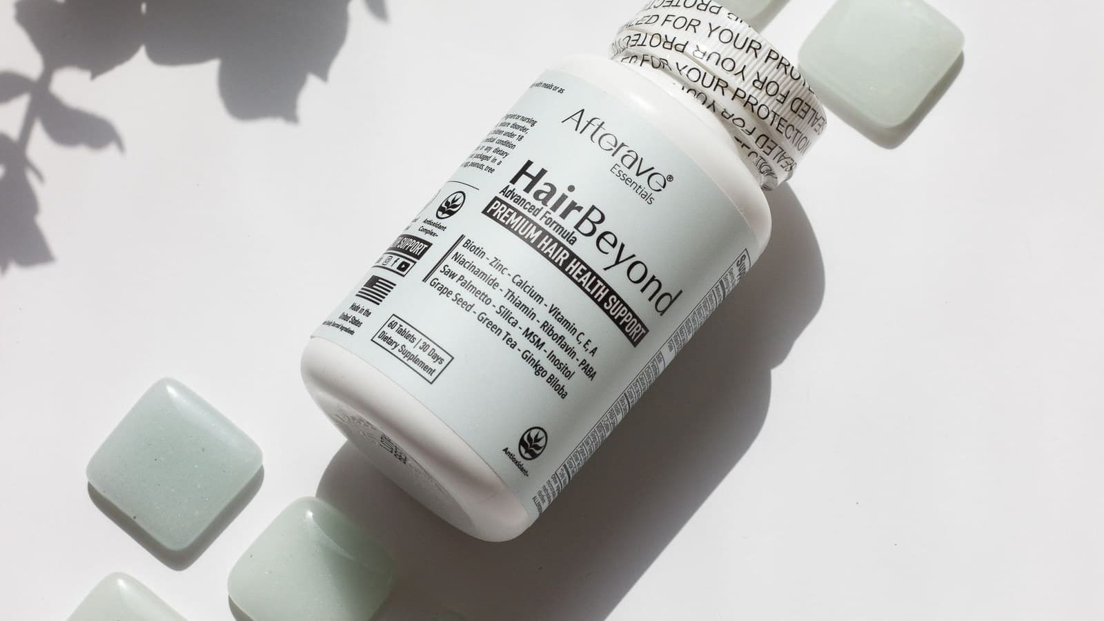 Hair growth supplement bottle with green tablets on a white surface